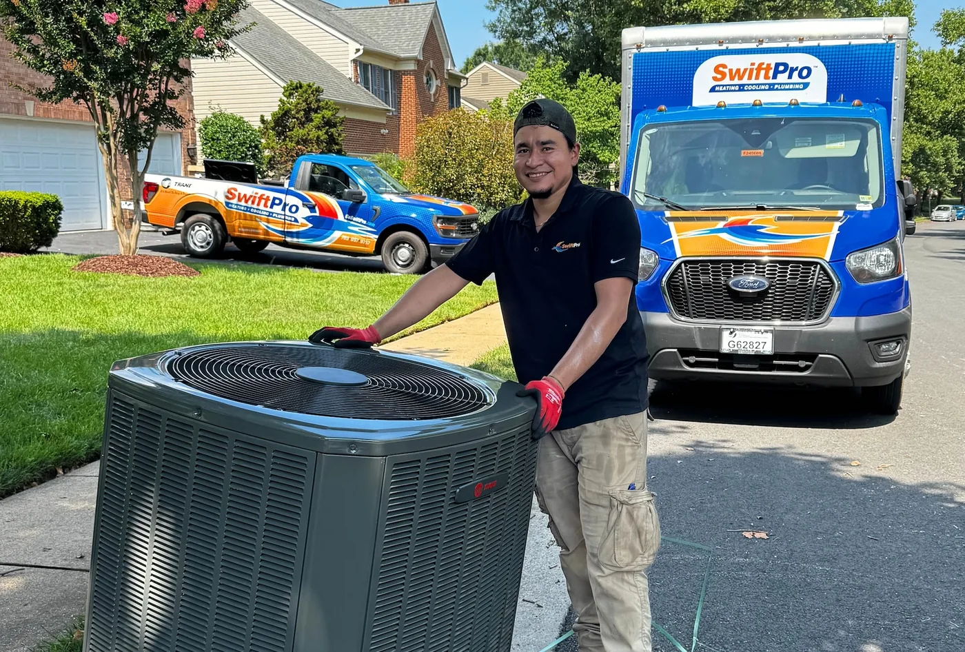 SwiftPro technician beside an outdoor air-conditioning unit, with SwiftPro trucks in the background