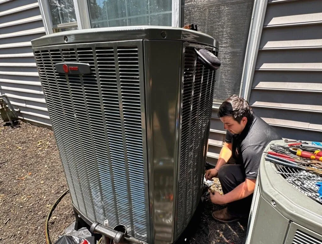 SwiftPro technician working on an outdoor air-conditioning unit beside a home